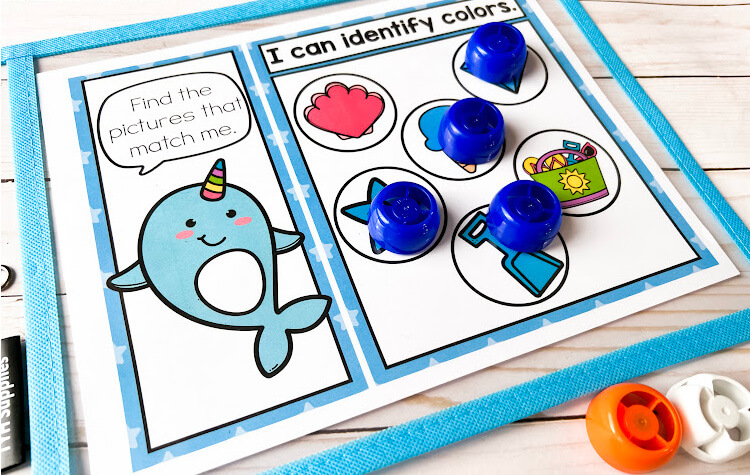 Free printable narwhal color matching worksheet for preschoolers. Blue narwhal shows with blue star, blue shovel, blue ice cream and blue gem covered by small manipulatives.